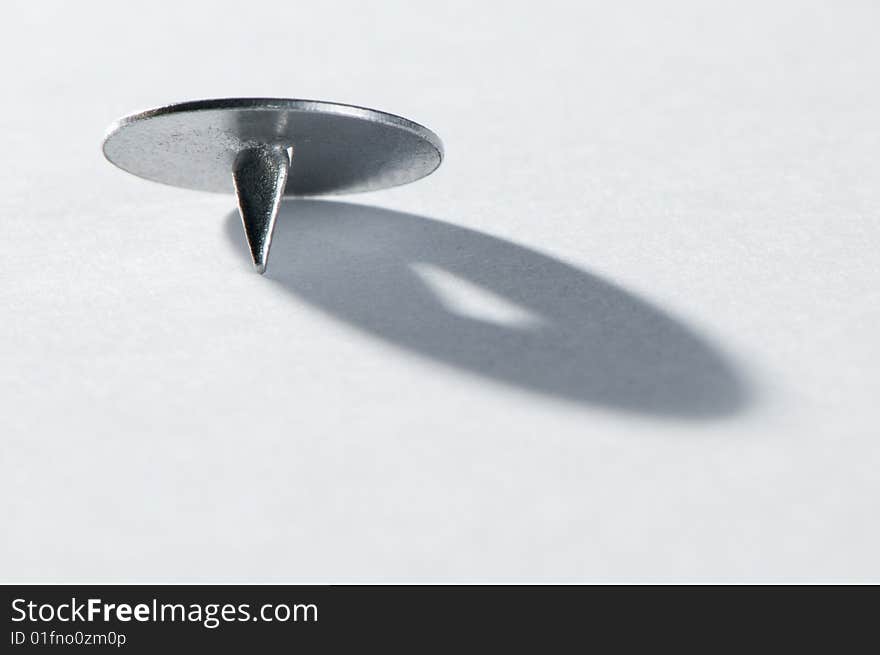 Old-style steel pushpin on white paper casting a shadow. Old-style steel pushpin on white paper casting a shadow