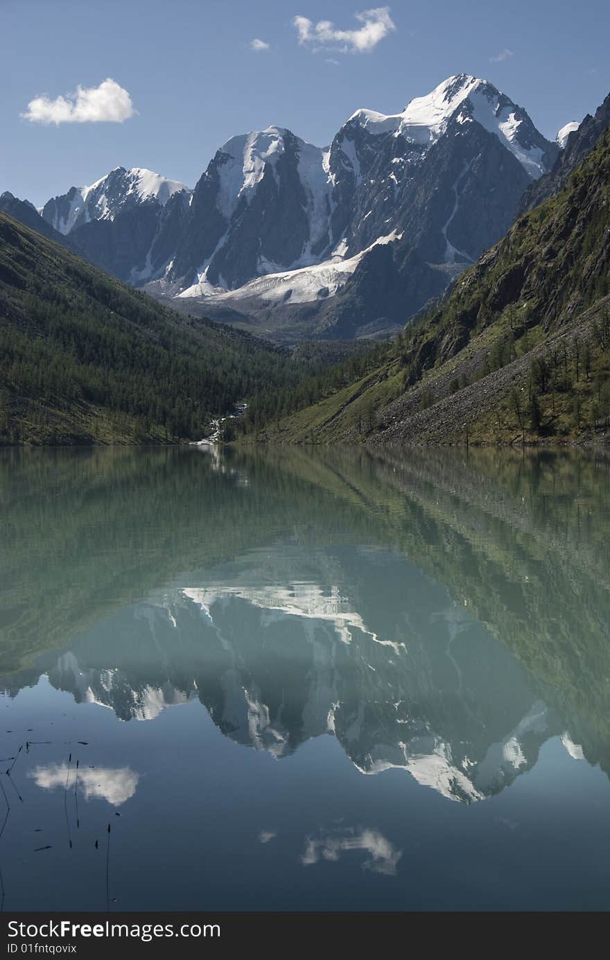 Shining snowy peak and blue sky with reflection in the mountain lake. Shining snowy peak and blue sky with reflection in the mountain lake