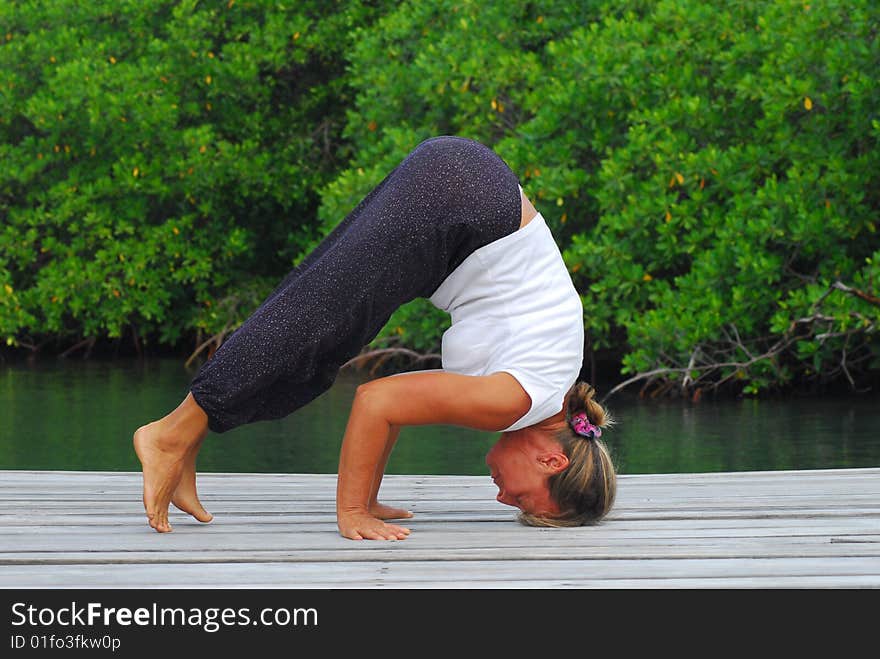 Woman doing yoga on wooden dock with green mangrove behind  her.