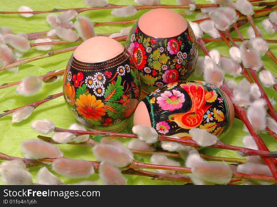 Three easter eggs and sprig of flowering willow on a background to the green paper