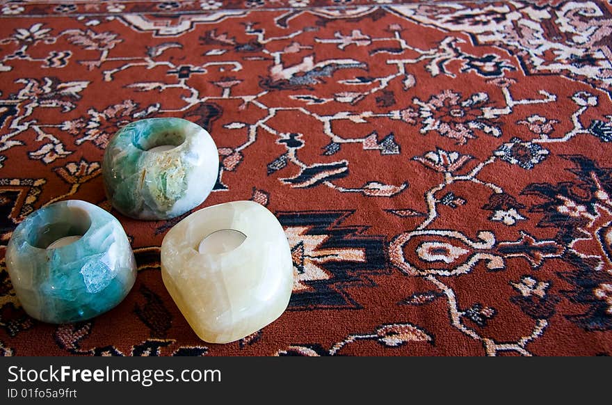 Three stone candle holders with three unlit candles in them on a decorative cloth