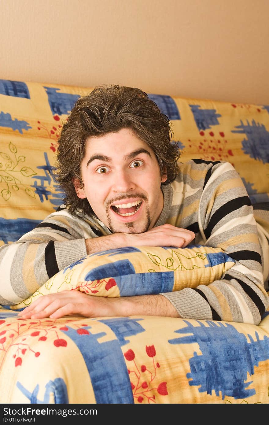 Young dark haired caucasian man in striped sweater lying on country style sofa ��� laughing. Young dark haired caucasian man in striped sweater lying on country style sofa ��� laughing