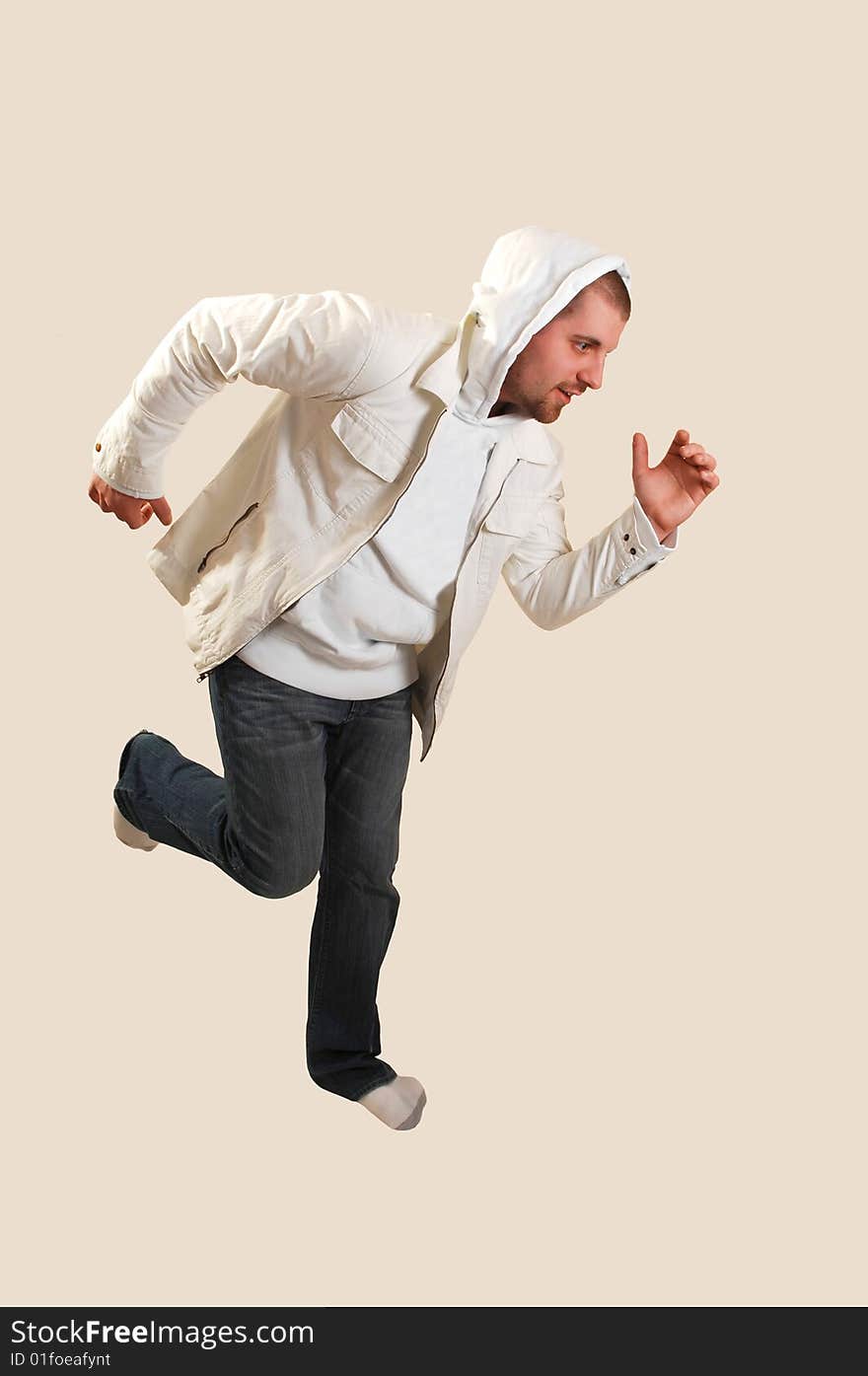 A young athletic man posing running in the studio with an white jacket and the hood over his head, on beige background. A young athletic man posing running in the studio with an white jacket and the hood over his head, on beige background.