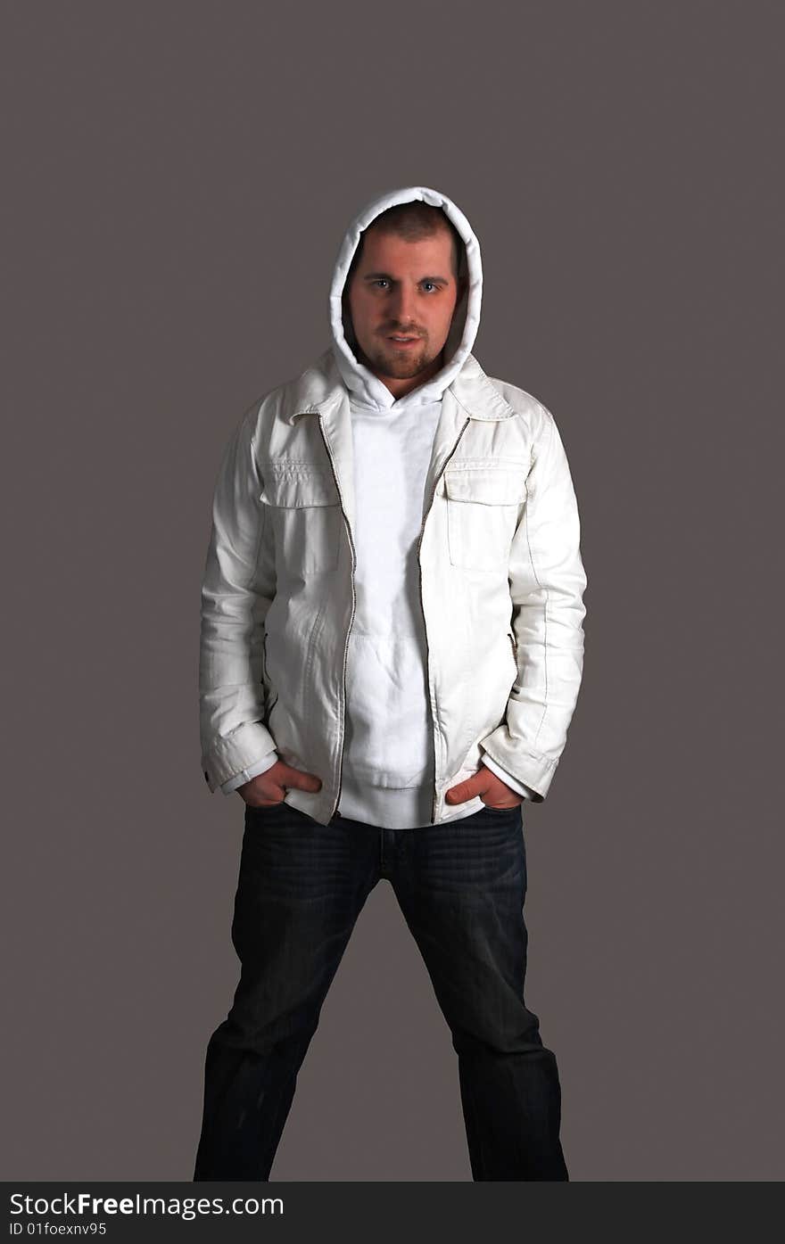 An young man with his hands in the pocket and a white jacket with a hood
on his head for dark gray background. An young man with his hands in the pocket and a white jacket with a hood
on his head for dark gray background.