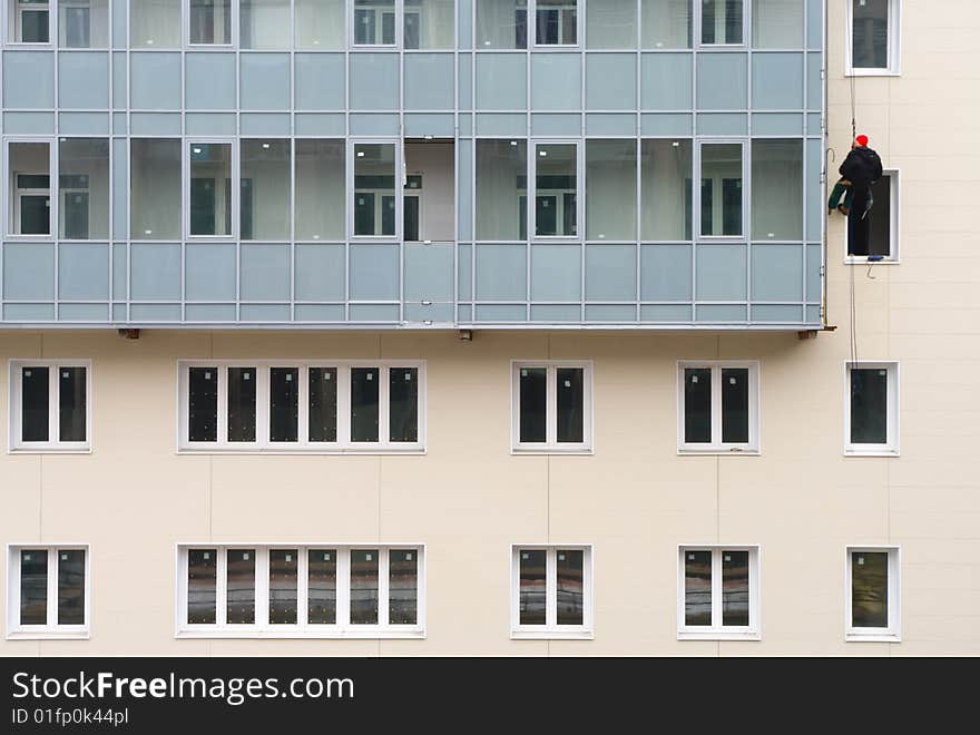 Beige facade of building under construction with many windows and balconies. The alpinist working on the facade suspended on the cord. Beige facade of building under construction with many windows and balconies. The alpinist working on the facade suspended on the cord.