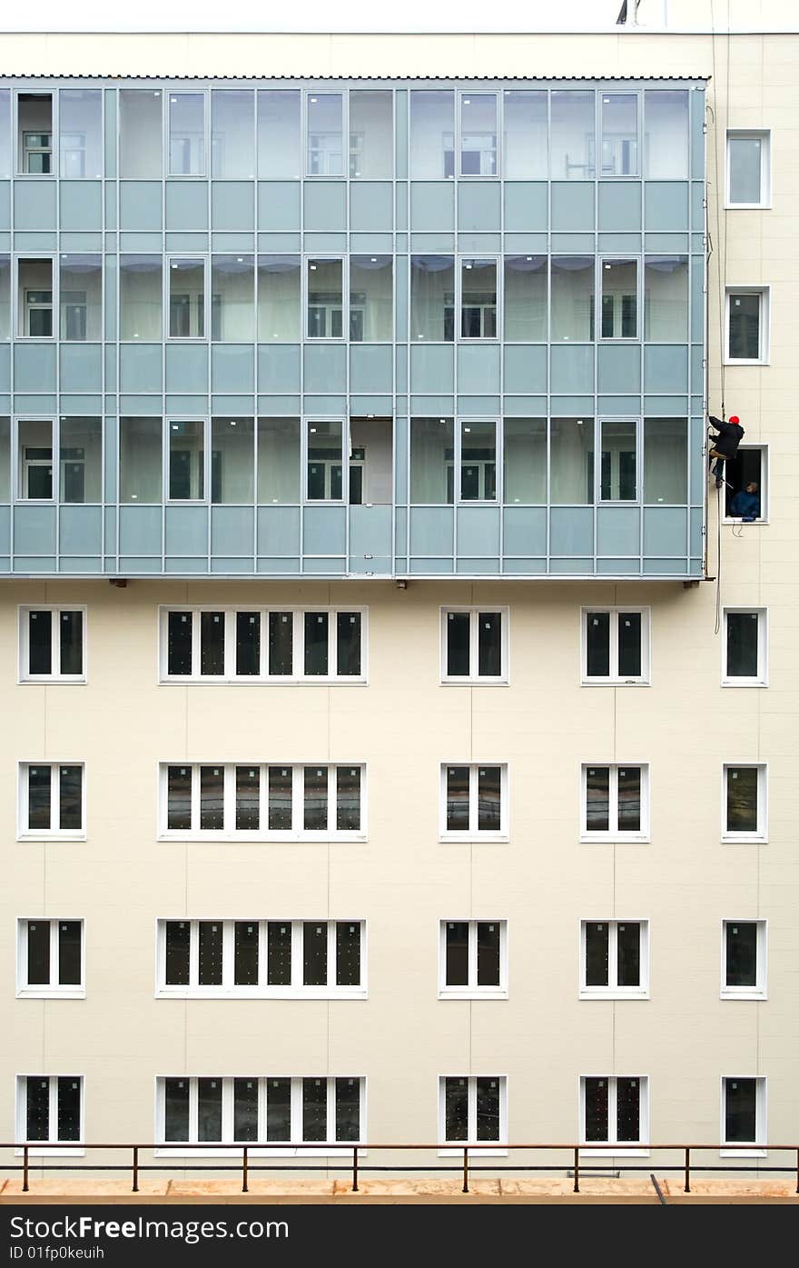 Beige facade of building under construction with many windows and balconies. The alpinist working on the facade suspended on the cord. Beige facade of building under construction with many windows and balconies. The alpinist working on the facade suspended on the cord.