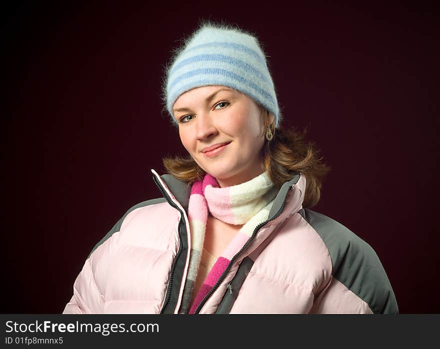 Pretty female model wearing women's outdoor winter ski clothing with a fuzzy pastel blue hat on a dark red background. Pretty female model wearing women's outdoor winter ski clothing with a fuzzy pastel blue hat on a dark red background