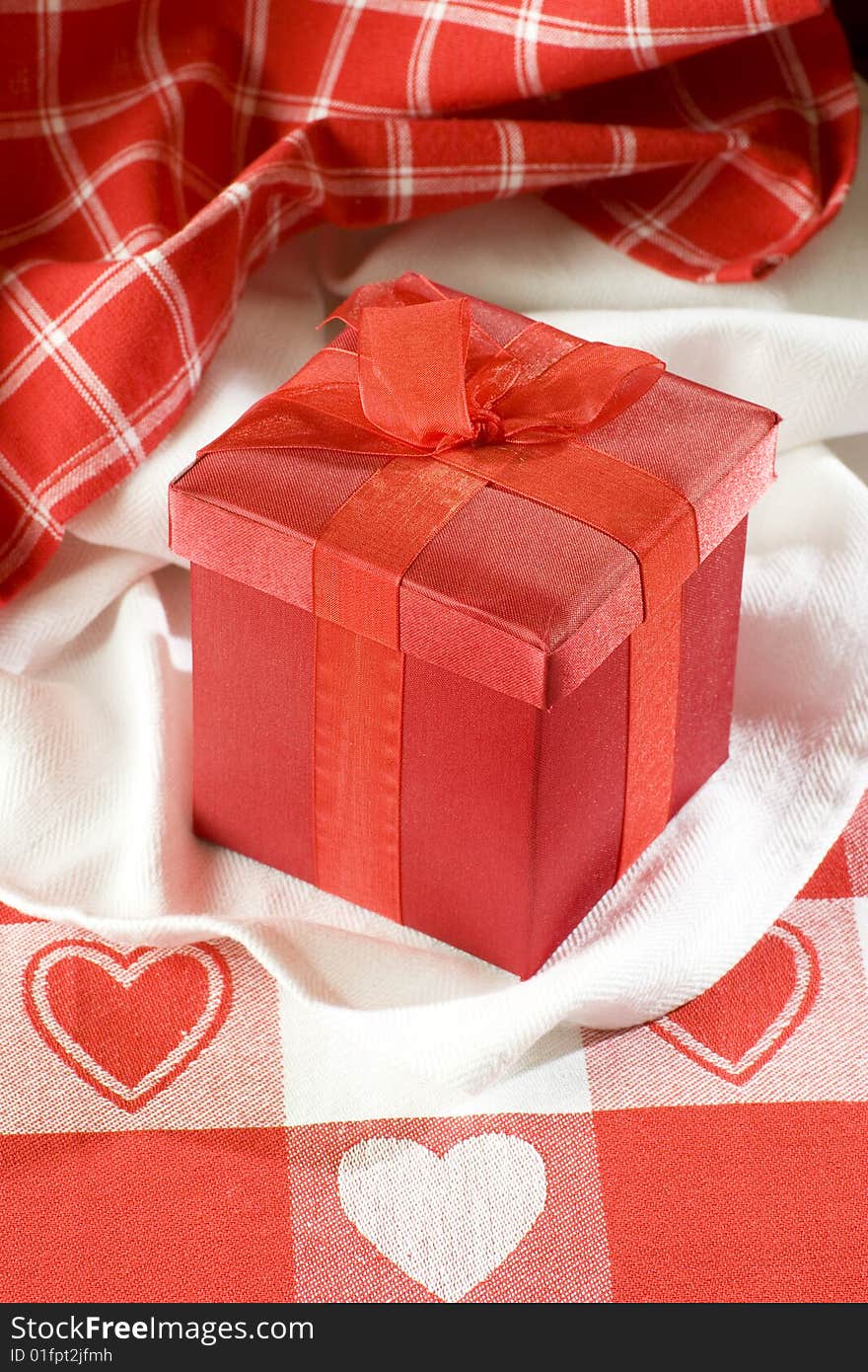 Red Valentines gift box on table cloth with red hearts. Red Valentines gift box on table cloth with red hearts