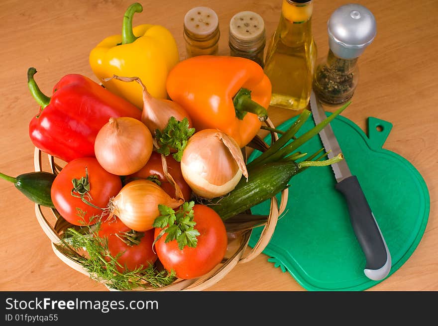 Crude vegetables in a basket, a chopping board, a knife, olive oil and spices. Crude vegetables in a basket, a chopping board, a knife, olive oil and spices.