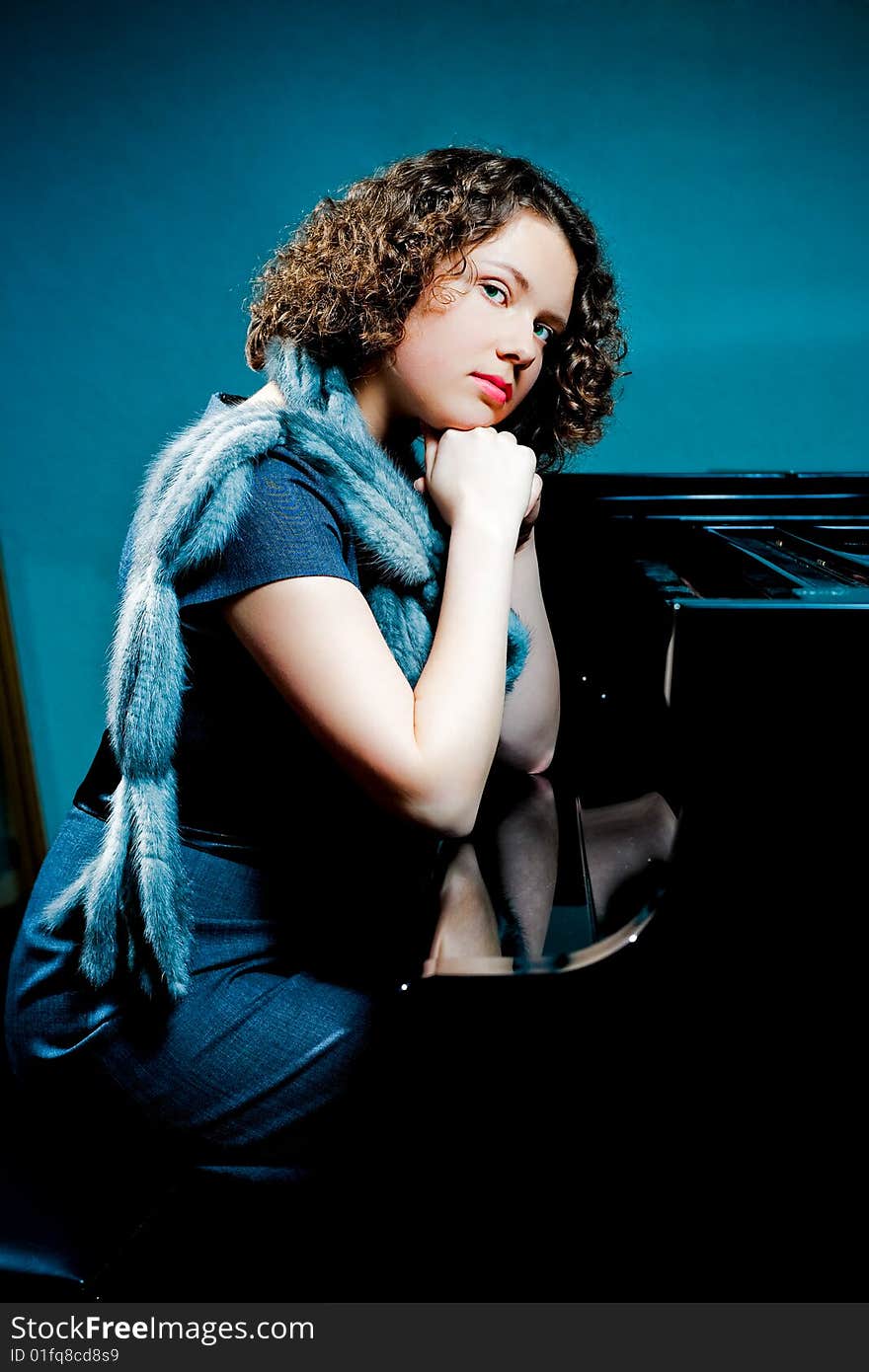 Pretty young dark haired girl sitting near piano with hands ctossed in front looking forward with fur scarf and reflections on cover isolated. Pretty young dark haired girl sitting near piano with hands ctossed in front looking forward with fur scarf and reflections on cover isolated