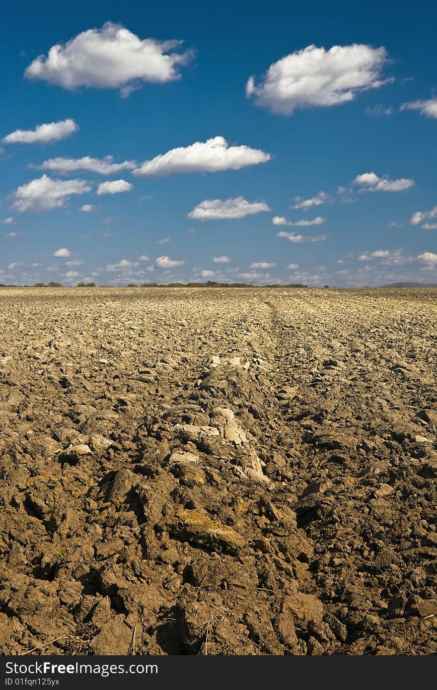 Rural landscape with the ploughed field and the dark blue sky with white clouds