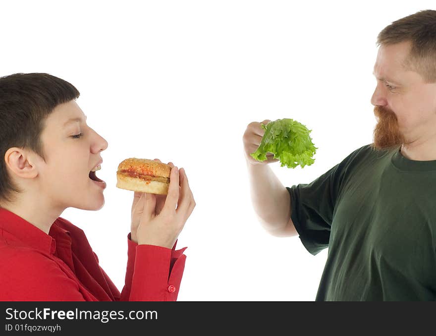 A woman is about to bite a hamburger while a breaded man standing beside her stares in surprise at lettuce leaves in his hand. A woman is about to bite a hamburger while a breaded man standing beside her stares in surprise at lettuce leaves in his hand