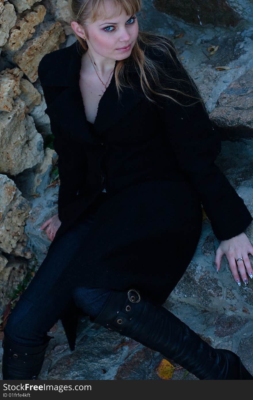 Beautiful young woman lies on the stairs in a black overcoat