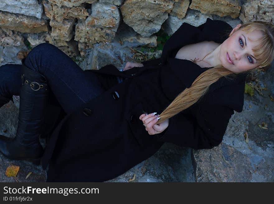 Beautiful young woman lies on the stairs in a black overcoat