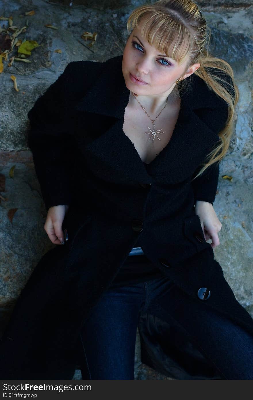 Beautiful young woman lies on the stairs in a black overcoat