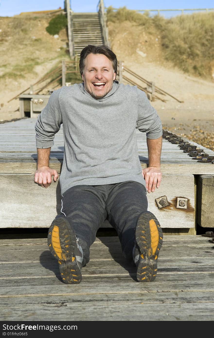 A happy forties man is performing strength exercises on the boardwalk at the beach. A happy forties man is performing strength exercises on the boardwalk at the beach.