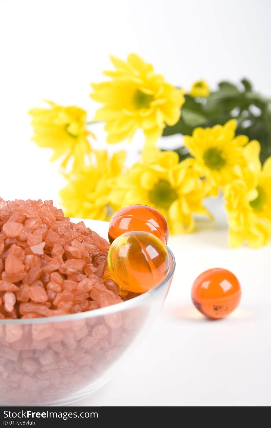 Spa pruducts: bath salt, oil balls in a bowl and yellow flowers