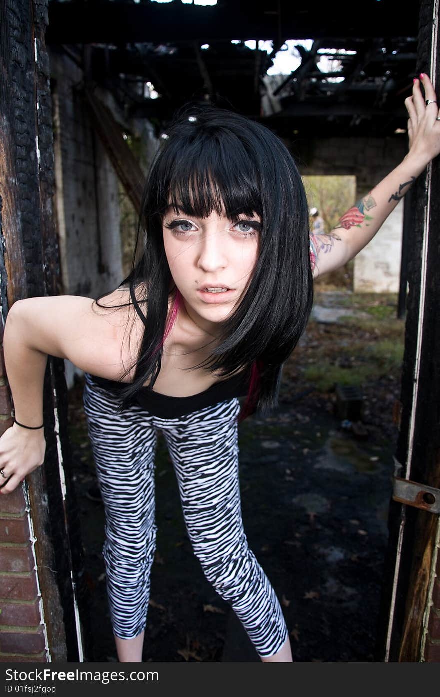 Pretty young woman with a left arm tattoo standing in a doorway of an abandoned building. Pretty young woman with a left arm tattoo standing in a doorway of an abandoned building