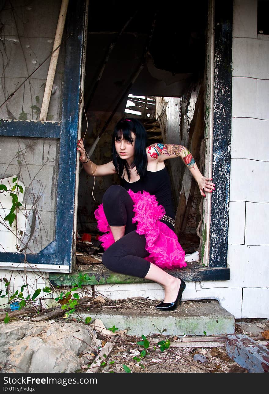 Pretty young woman with a left arm tattoo kneeling in a doorway of an abandoned building. Pretty young woman with a left arm tattoo kneeling in a doorway of an abandoned building