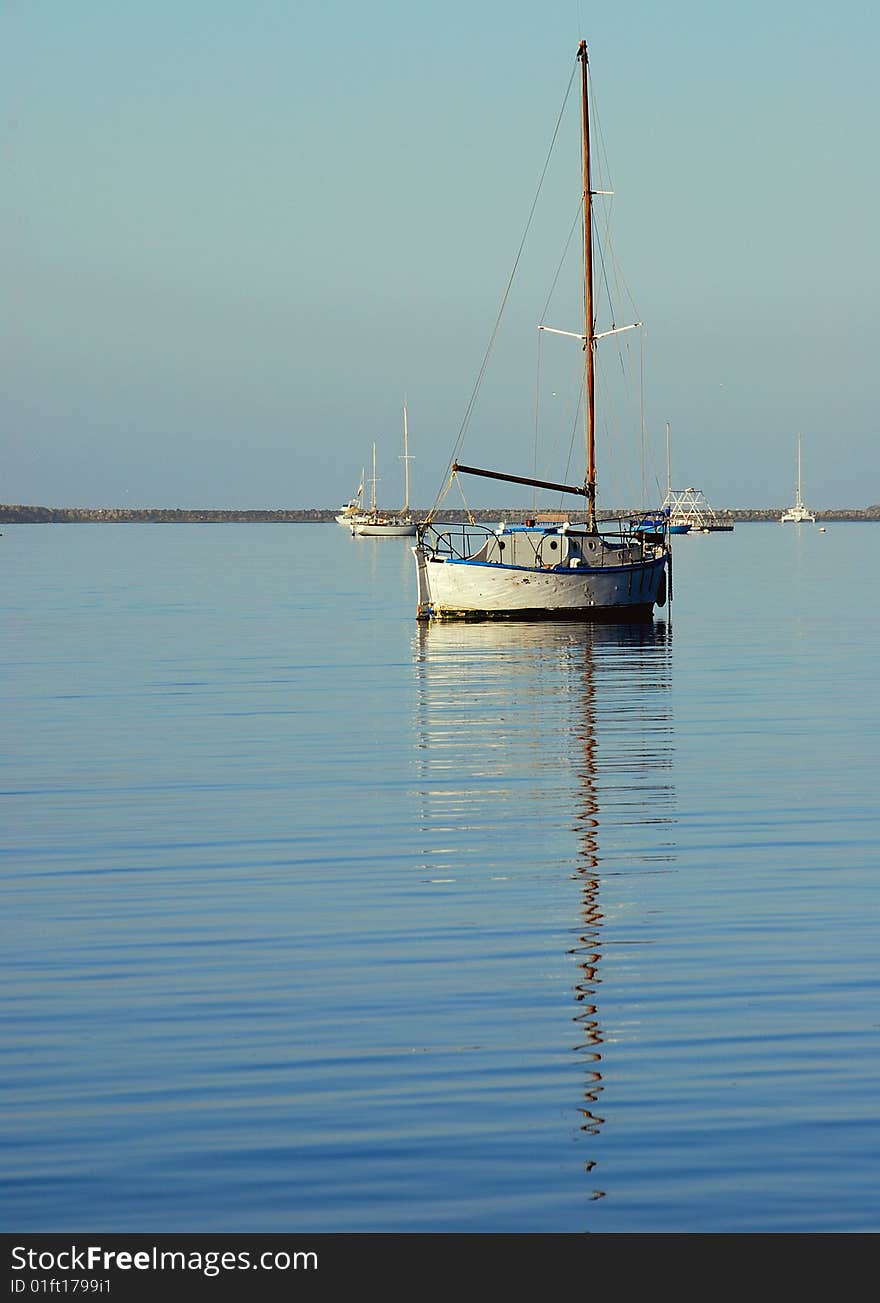 Small wooden sloop and reflection in a calm anchorage on a still day. Small wooden sloop and reflection in a calm anchorage on a still day.