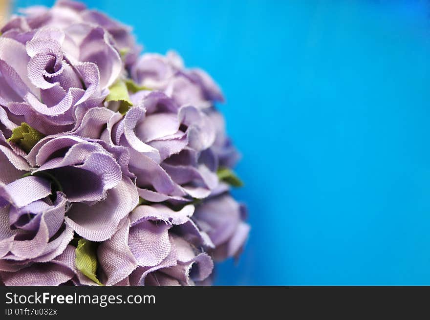 Fake purple flowers against blue background with a space for a text. Fake purple flowers against blue background with a space for a text