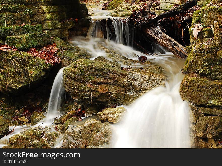 This image is of a small set of rapids downstream of a larger falls. The image shows some large rocks with green moss growing on them.