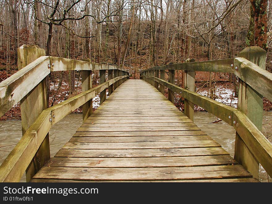 This is a shot of a wooded bridge walkway over a river. A little bit of the river can be seen on either side of the bridge. Woods can be seen on the opposite side of the walkway. This is a shot of a wooded bridge walkway over a river. A little bit of the river can be seen on either side of the bridge. Woods can be seen on the opposite side of the walkway.