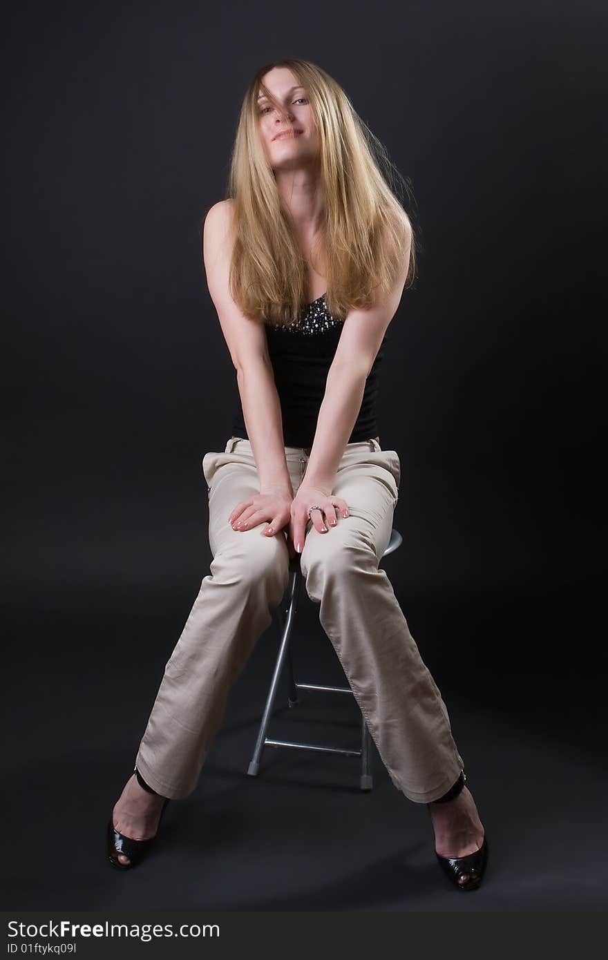 Beautiful girl sits on a chair against a dark background. Beautiful girl sits on a chair against a dark background