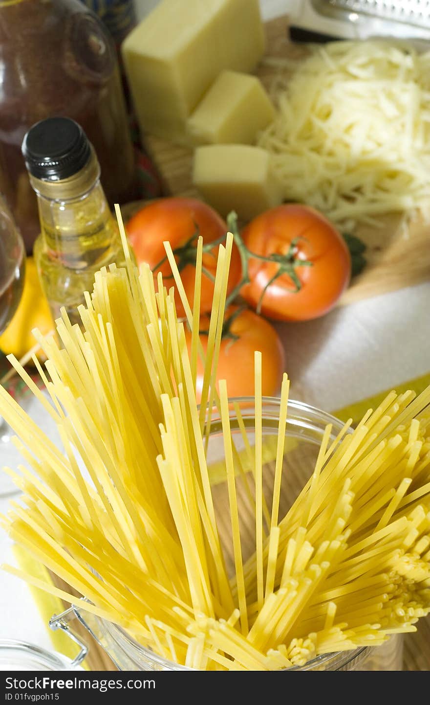 Overhead shot of ready for cooking spaghetti in glass container with tomatoes and cheese in the background. Overhead shot of ready for cooking spaghetti in glass container with tomatoes and cheese in the background