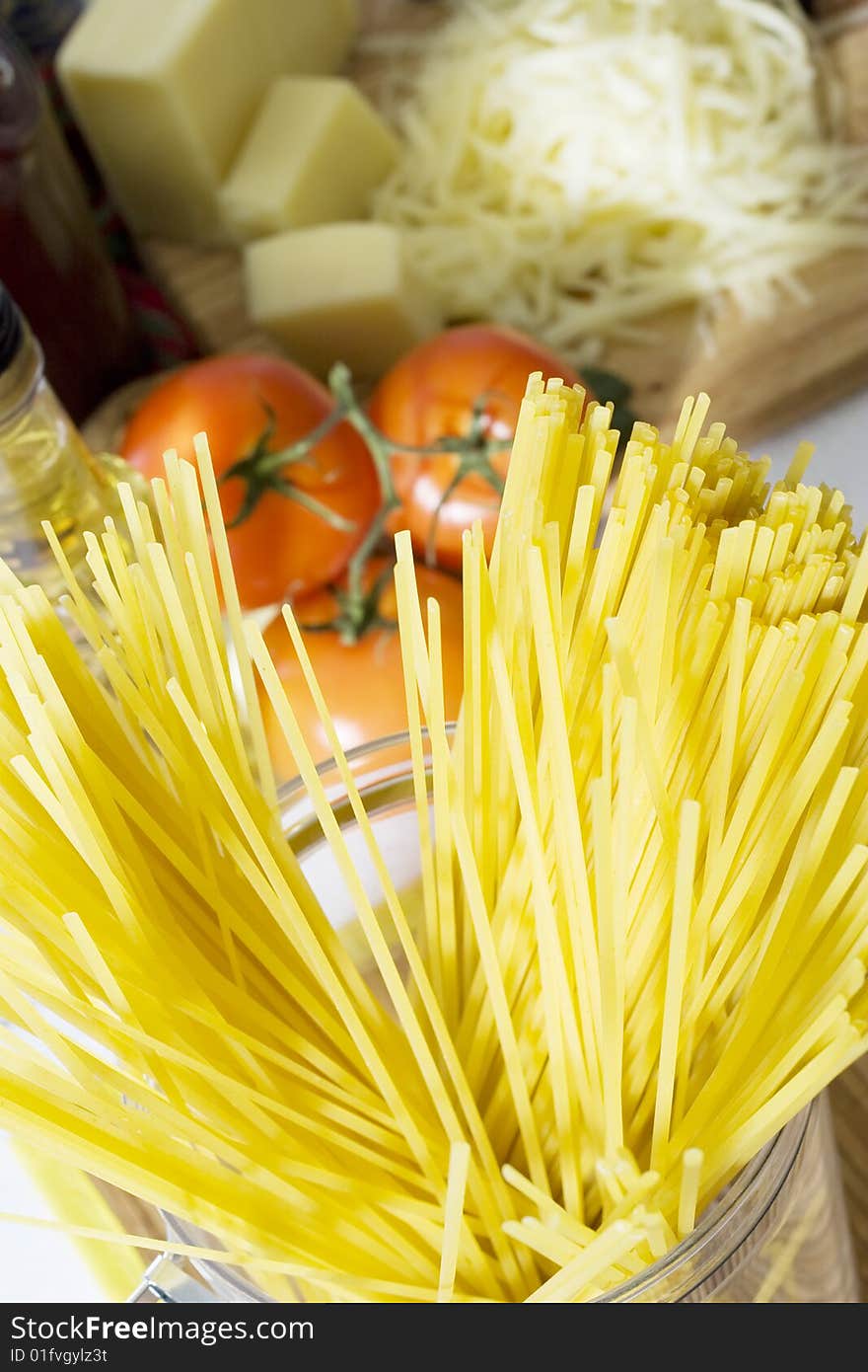 Overhead shot of ready for cooking spaghetti in glass container with tomatoes and cheese in the background. Overhead shot of ready for cooking spaghetti in glass container with tomatoes and cheese in the background