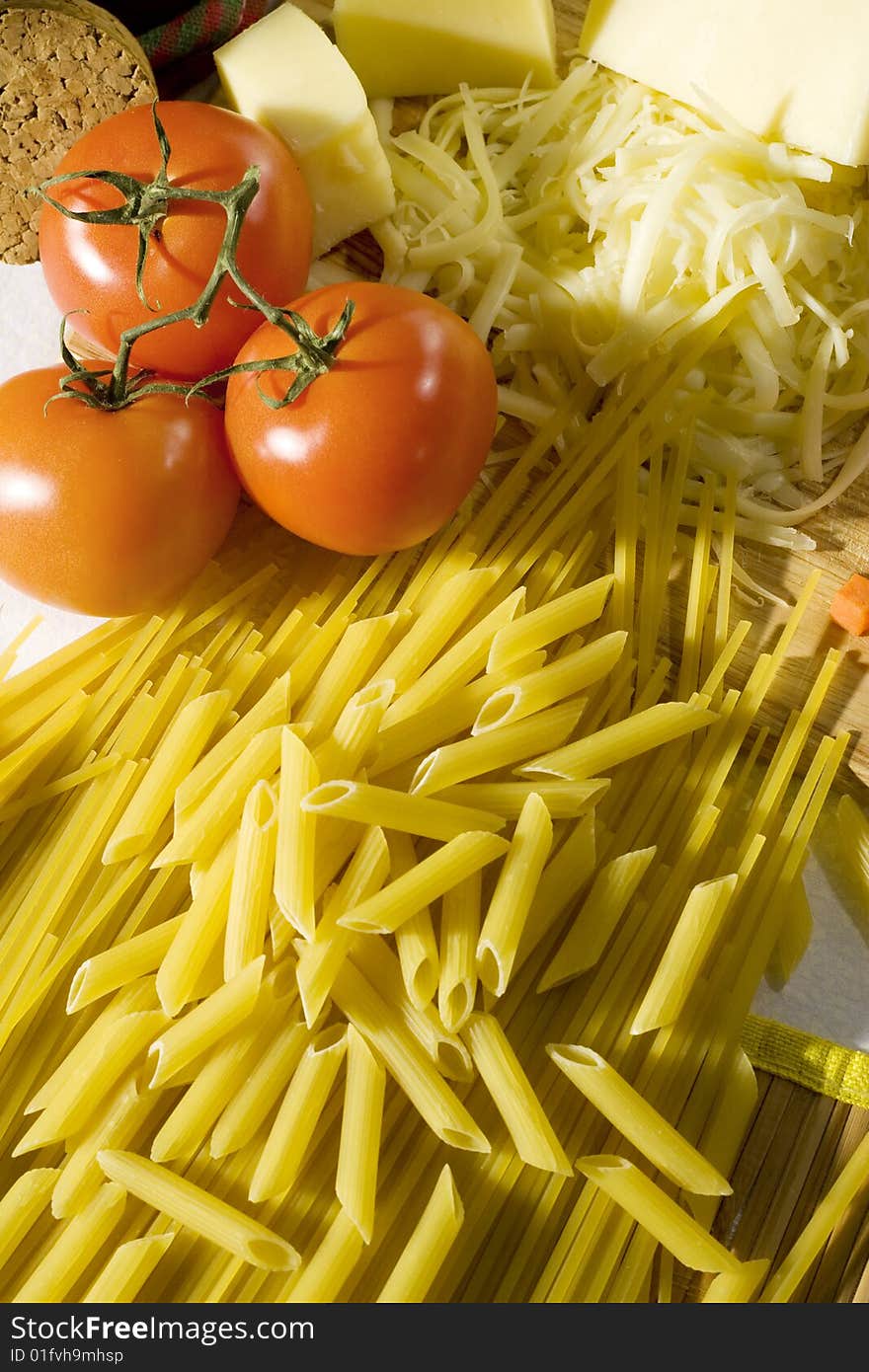 Overhead shot of raw spaghetti and macaroni next to a tomatoes and grated cheese