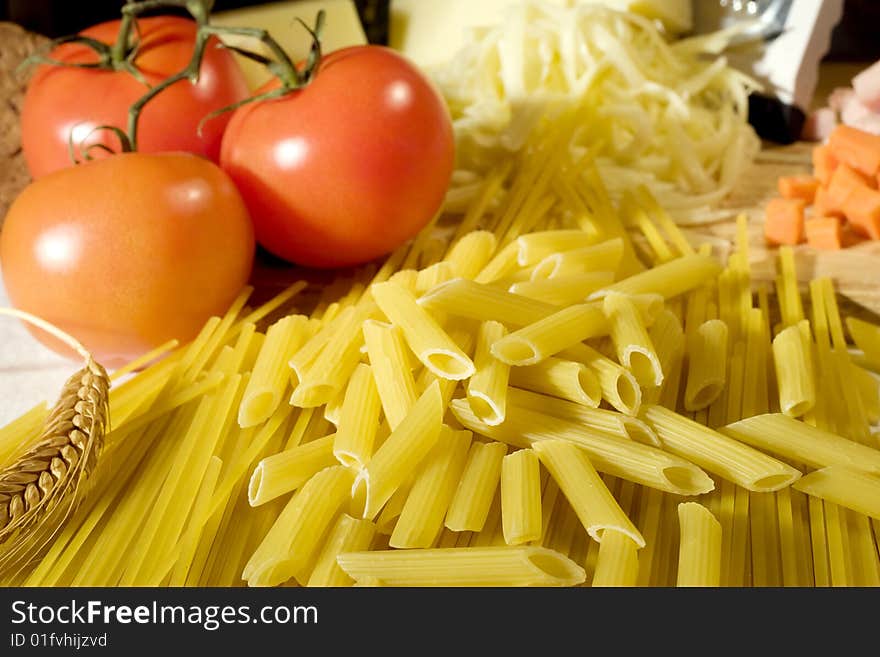 Overhead shot of raw spaghetti and macaroni next to a tomatoes and grated cheese