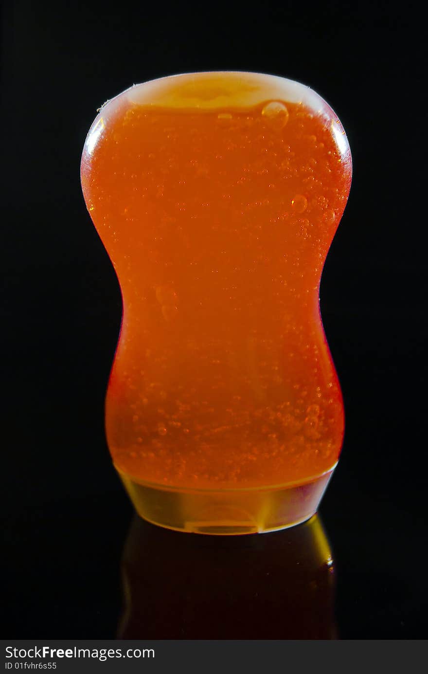 A clear isolated 3oz TSA approved bottle filled with a orange bath gel on a black background. A clear isolated 3oz TSA approved bottle filled with a orange bath gel on a black background