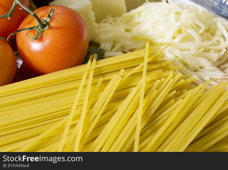 Overhead shot of raw spaghetti next to a tomatoes and grated cheese