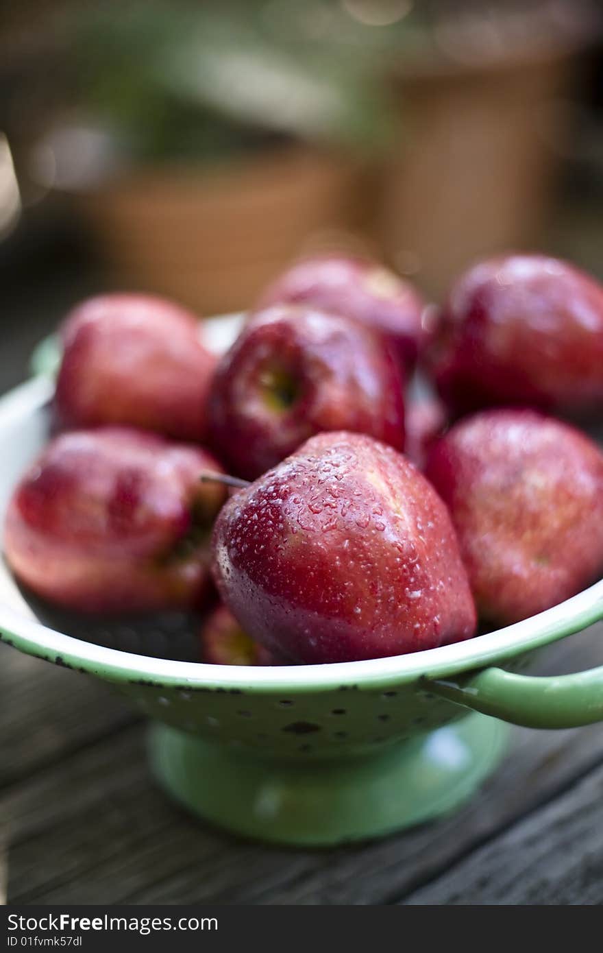 Apples sprayed with water placed in a basket strainer on an old wood tabletop.