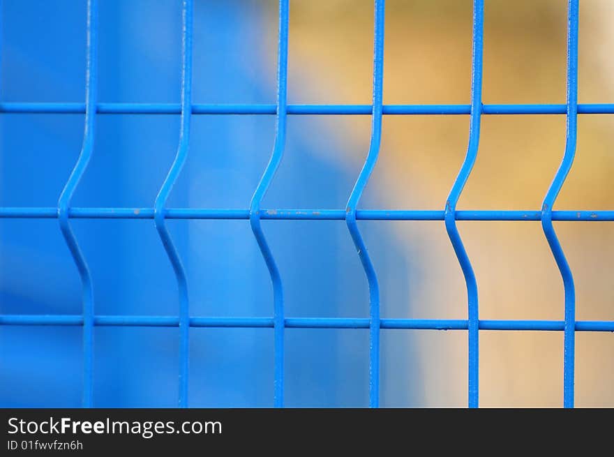 Close up of blue metal fence with blurred blue and orange background. Close up of blue metal fence with blurred blue and orange background