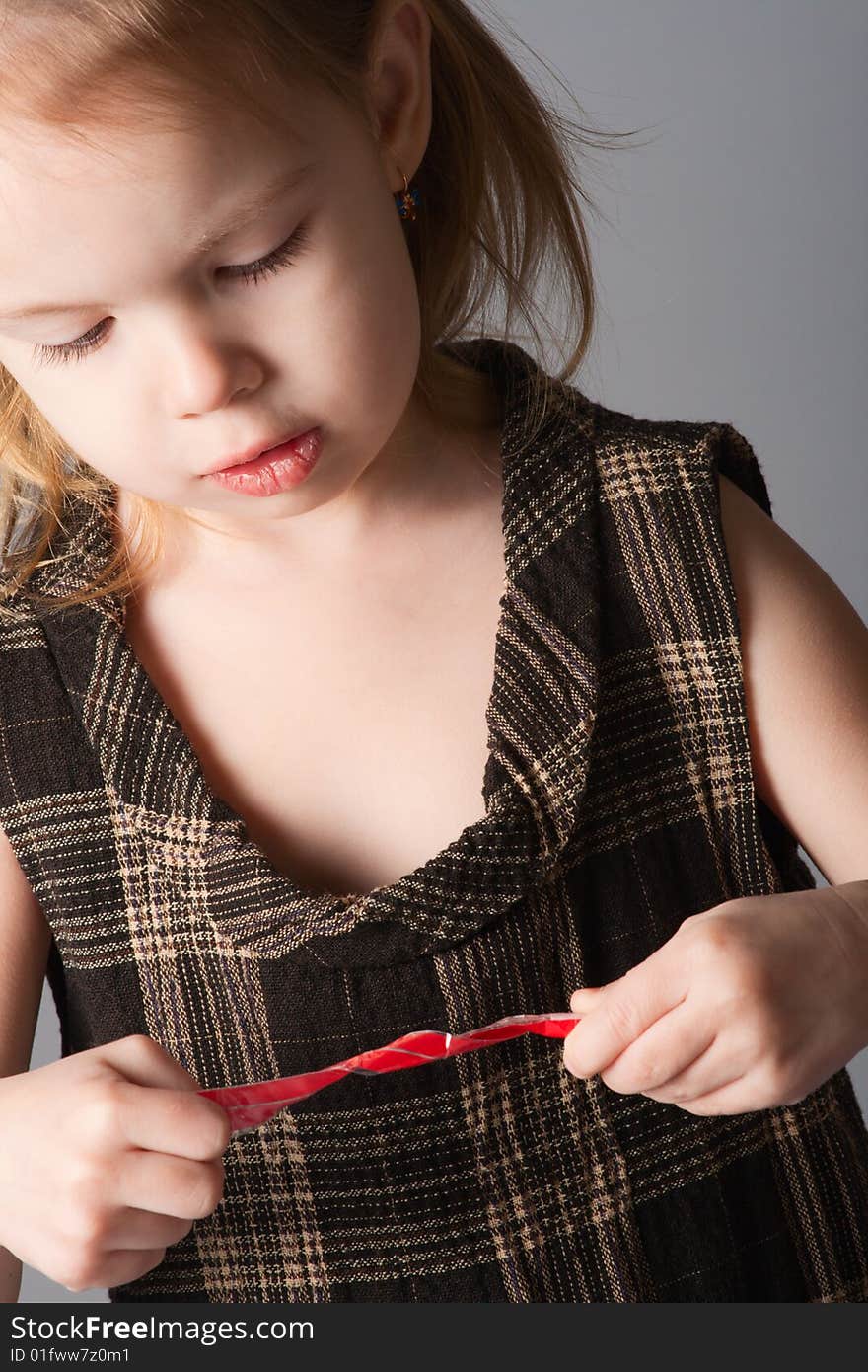 Little beauty girl look at red ribbon in her hands. She lowers her long black eyelashes. Little beauty girl look at red ribbon in her hands. She lowers her long black eyelashes.