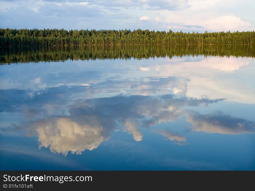 In lake in calm water is reflected wood and cloud. In lake in calm water is reflected wood and cloud