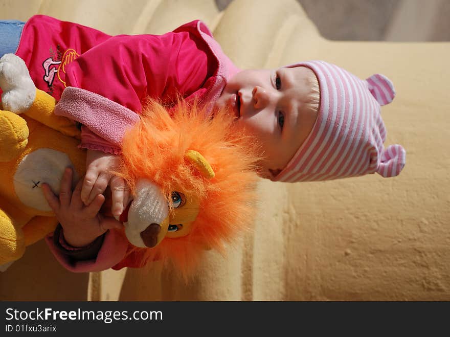 Little girl in a brightly red jacket with a toy lion cub in hands on a yellow background