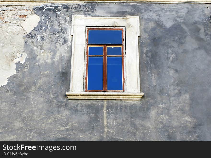 The wall of an old building with a window in which is reflected the  blue sky