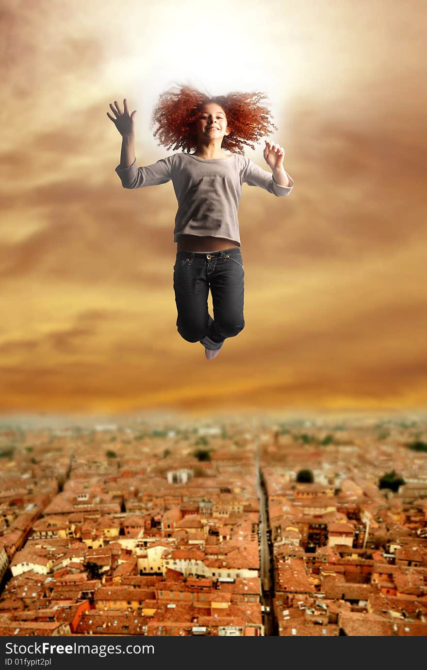 A young girl jumping with an aereal view of a village on the background