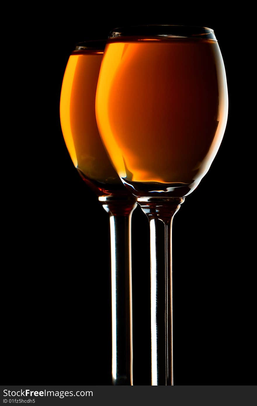 Two small glasses filled with orange liquor on black background. Two small glasses filled with orange liquor on black background