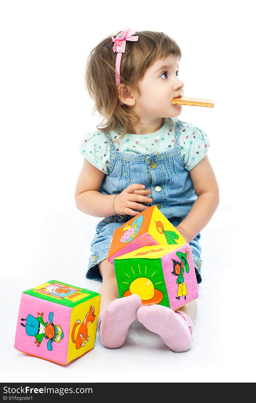 Cute one year old girl playing with her toys on the floor and eating a cookie