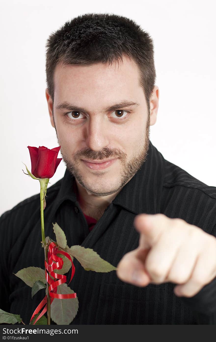 Young, handsome man, holding a red rose, pointing his finger and looking at the camera, smiling. Young, handsome man, holding a red rose, pointing his finger and looking at the camera, smiling