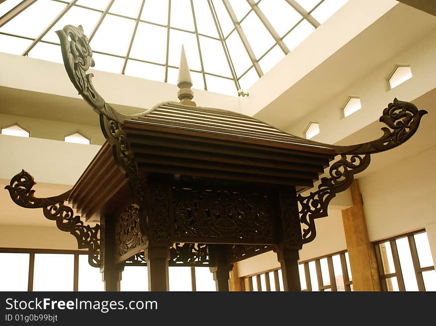 An Asian handcrafted gazebo rooftop under the glass rooftop of a shopping mall.