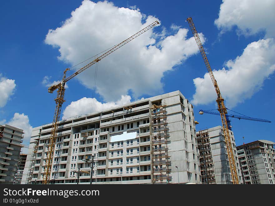 Cranes on construction site and blue sky with clouds in background.