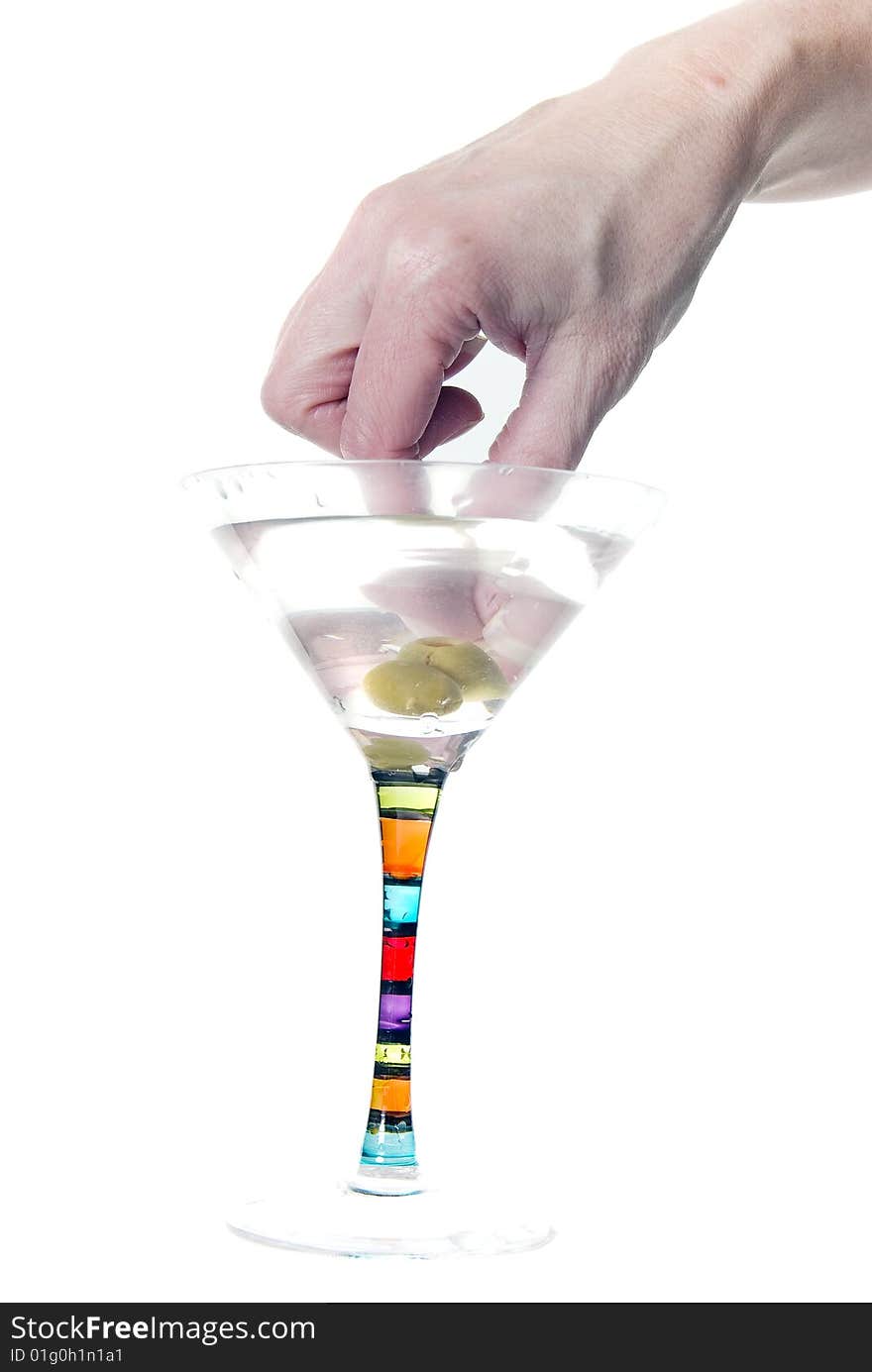 A female hand dips into martini to pluck out two olives on a toothpick. A female hand dips into martini to pluck out two olives on a toothpick