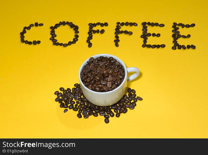 Coffee written with beans on yellow background.  Cup on foreground.