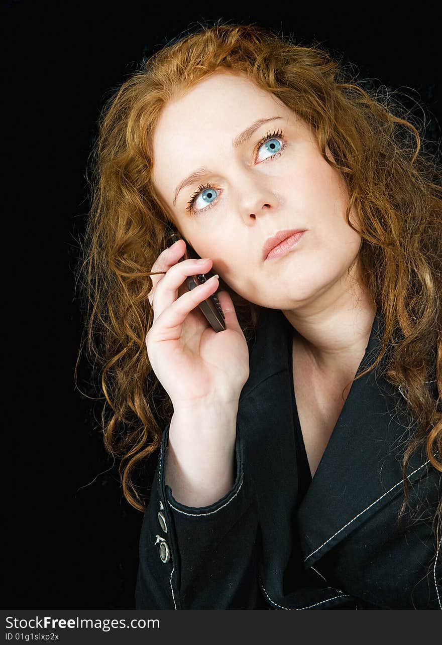 Beautiful girl with red hair speaking in mobile phone, seen against black background. Beautiful girl with red hair speaking in mobile phone, seen against black background