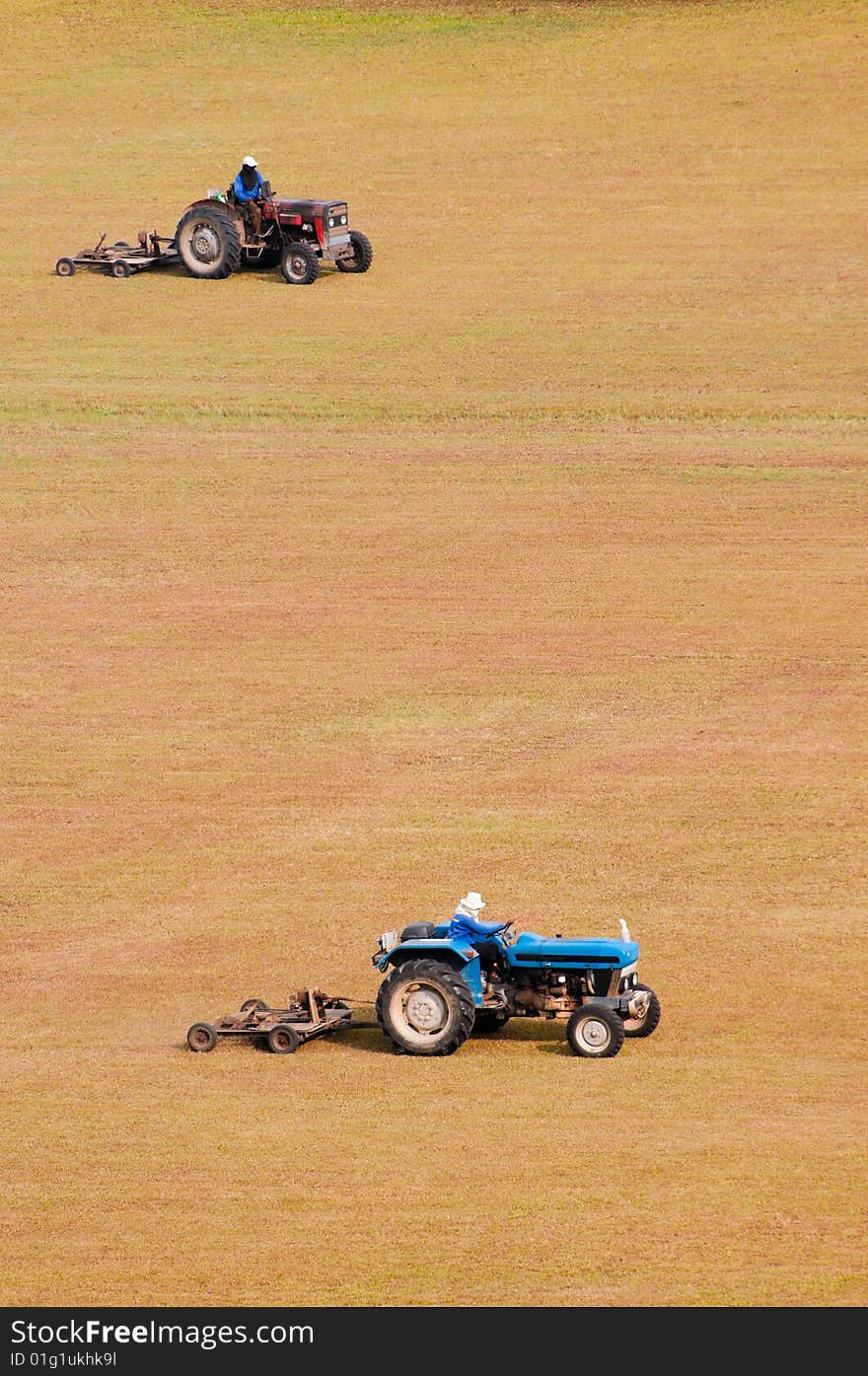 A pair of tractor-towed mowers moving a large open flat dry field. A pair of tractor-towed mowers moving a large open flat dry field